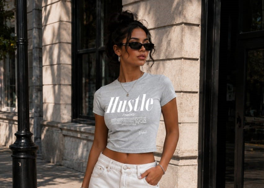 Woman wearing a gray 'Hustle' t-shirt and white pants standing on a street.